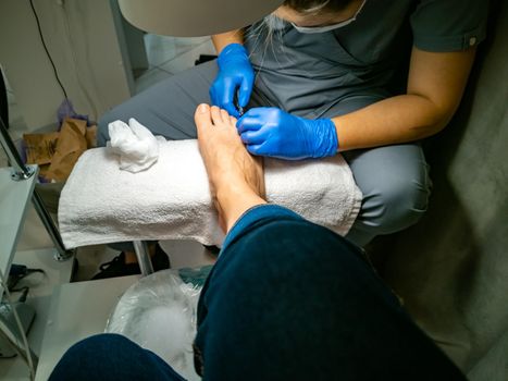 a gloved master makes a pedicure for a client. close-up no face. woman in a nail salon paints her nails with red varnish