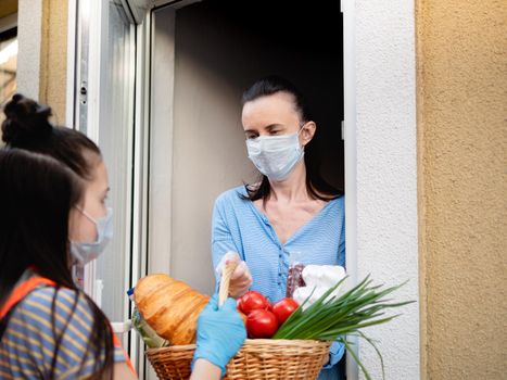 Food delivery during a pandemic and strict quarantine. A teenage volunteer girl delivered a basket of food to a woman in strict isolation.