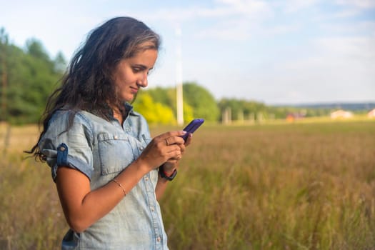 happy young woman looks into smartphone on nature background on sunny day