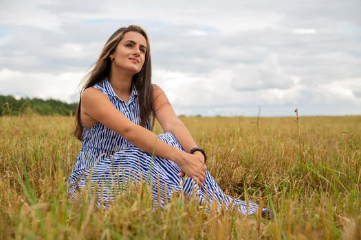 beautiful young woman sits in a meadow in flowers on a sunny summer day and smiles.