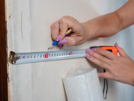 A woman makes measurements on the wall for wallpapering with a measuring ruler.