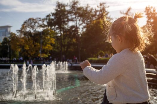 adorable little girl looks at the fountain. toddler in a park with fountains on a sunny day.. family weekendю little girl looking into a fountain in the park