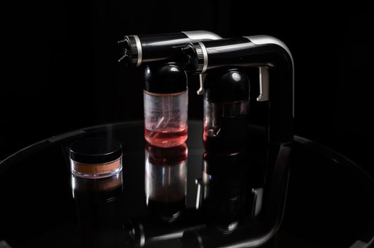 A close-up of the instant tanning equipment. Gun spraying paint for leather, brush and matting body powder on a black background