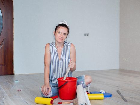 A woman stirs glue in a red bucket for wallpapering in an apartment.