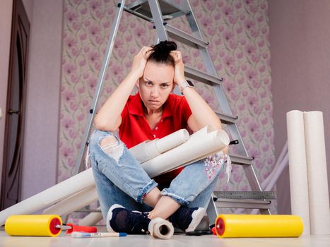 A woman is sitting on the floor and clutching her head from the volume of work of the upcoming renovation in the apartment.