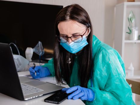 Serious woman in a medical mask sits on the workplace at the clinic.