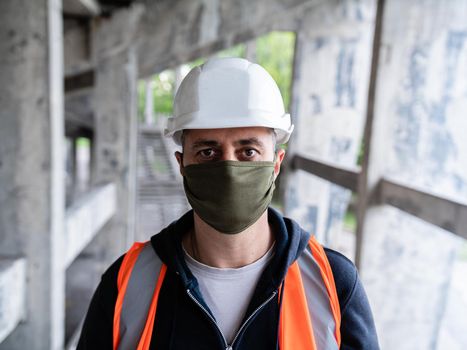 Close-up of a male construction worker in a construction helmet and protective medical mask on a construction site. Gradual exit from quarantine. The opening of the construction sites.