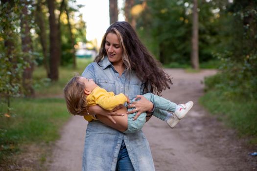 young mother is spinning with a baby in her arms. happy mom dancing with toddler on the background of nature and forest. mom and daughter laugh. carefree parenthood