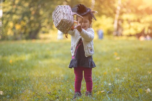 little toddler witch playing with a basket of leaves in autumn park