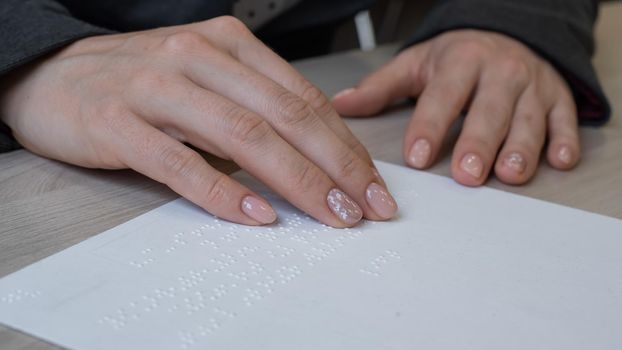 Close-up woman reads the text to the blind. Woman's hands on paper with braille code