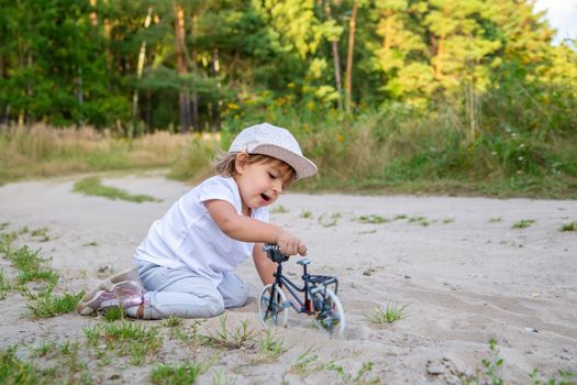 adorable toddler plays with a toy bike in nature. child on all fours in the sand on the lawn.