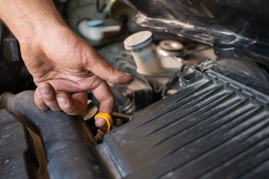 An auto mechanic pulls out a dipstick to check the oil level in a car engine