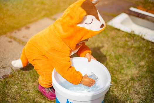 adorable little toddler playing with water in the backyard in sunshine. child in a fox costume