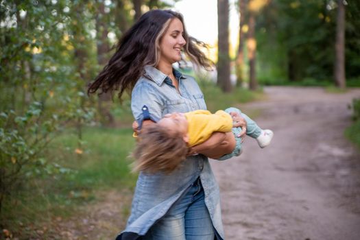 young mother is spinning with a baby in her arms. happy mom dancing with toddler on the background of nature and forest. mom and daughter laugh. carefree parenthood