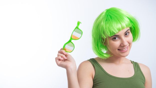 Cheerful young woman in green wig and funny glasses celebrating st patrick's day on a white background.
