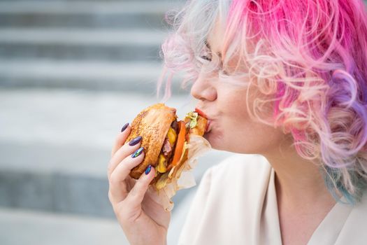 Caucasian woman with curly colored hair eating burger. Bad eating habits and love of fast food.