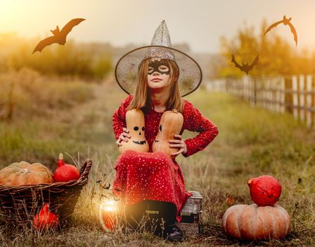 Little girl in halloween costume sitting next to pumpkins while frightening at camera on autumn nature