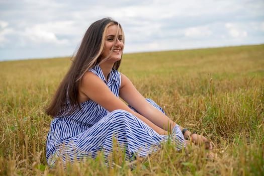 beautiful swarthy young woman sits in a meadow on a sunny day and enjoys the summer weather and wind.