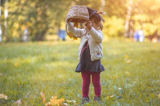 little cute witch flips a basket and pours autumn leaves in the park