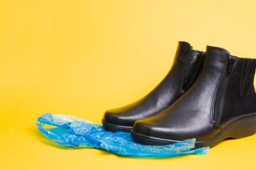 black leather boots and blue disposable shoe covers on a yellow background copy space