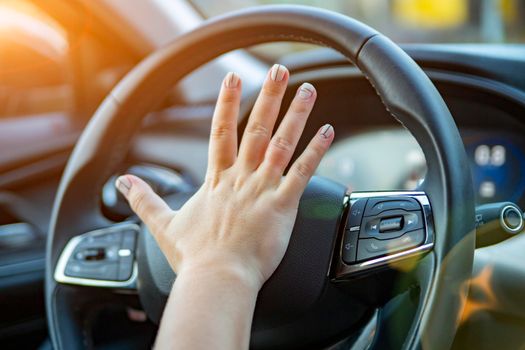 female hand presses the horn on the steering wheel of a modern car. no face