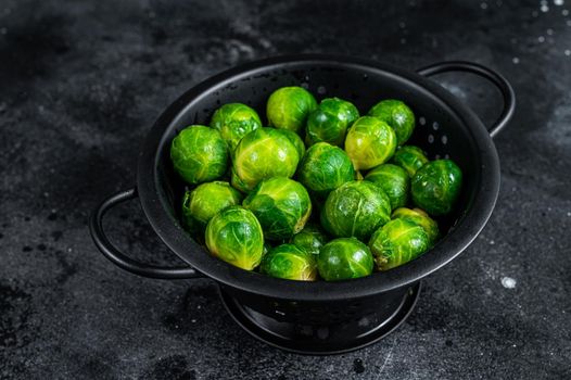 Brussels sprouts green cabbage in colander. Black background. Top view.