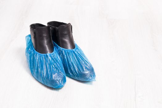 black leather boots in blue disposable shoe covers on a wooden light floor copy space