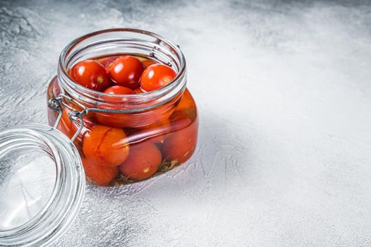 Pickled cherry tomatoes in a glass jar. White background. Top view. Copy space.