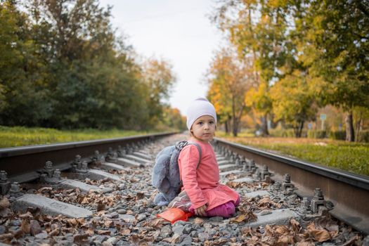 portrait of little girl sitting on the train tracks in the forest