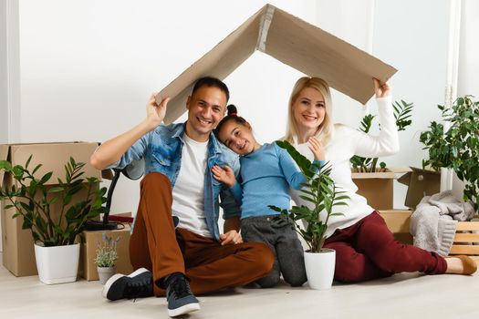 Happy family sitting on wooden floor. Father, mother and child having fun together. Moving house day, new home and design interior concept