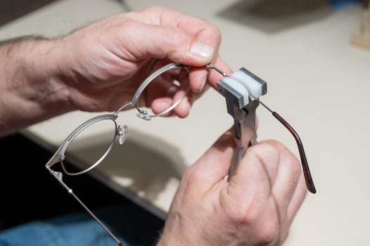 The man bends the temples of his glasses. The master repairs the frame with tongs