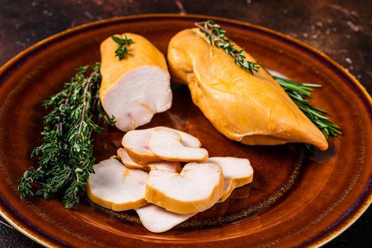 Hot Smoked chicken breast Poultry meat in a rustic plate with herbs. Dark background. Top view.