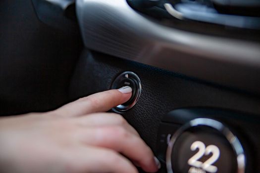 drivers hand finger presses the start stop button in a modern car. close-up. no face. keyless option in car. selective focus