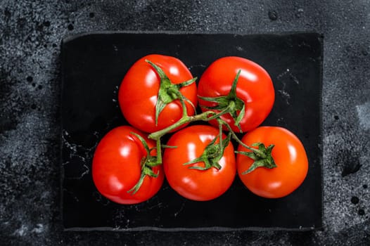 Branch of Red cherry tomatoes on marble board. Black background. Top view.