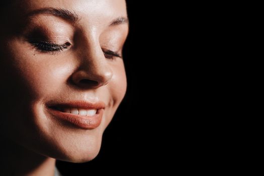 Portrait of a young European girl close-up on a black background in the evening light, close-up of a beautiful girl's face