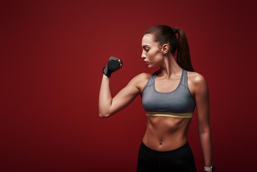 Portrait of a confident young fitness woman doing exercises with dumbbells isolated over red background. Studio shot