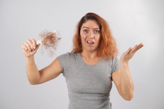 Caucasian woman with a grimace of horror holds a comb with a bun of hair. Hair loss and female alopecia