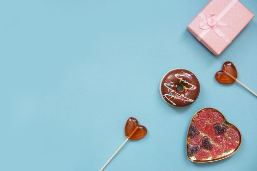 Lollipops in the form of hearts, a gift and greeting card on a blue background. Valentine's day, top view. Mortgage the apartment. Text phrase Love and Love is sweet.