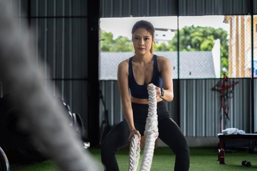 Female working out with battling rope at gym. Healthy modern people concept