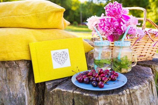 Picnic on the grass. Cherry, bouquet of flowers, fruit, book drinks