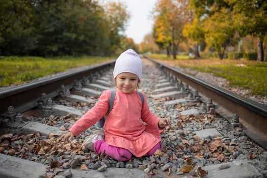 portrait of little girl sitting on the train tracks in the forest