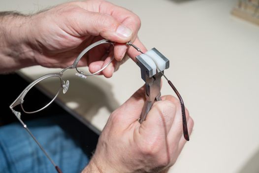 The man bends the temples of his glasses. The master repairs the frame with tongs