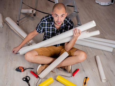 Portrait of a man on the floor with rolls of Wallpaper in his hands on the background of a stepladder.