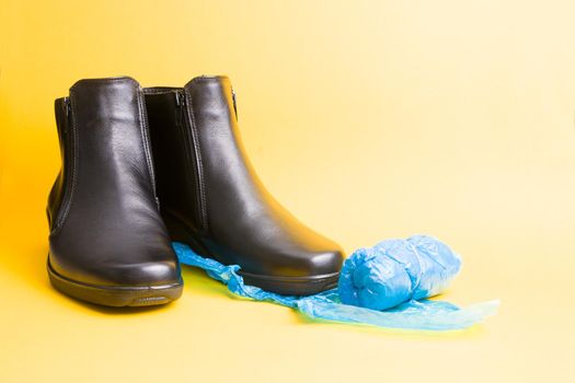 black leather boots and blue disposable shoe covers on a yellow background copy space