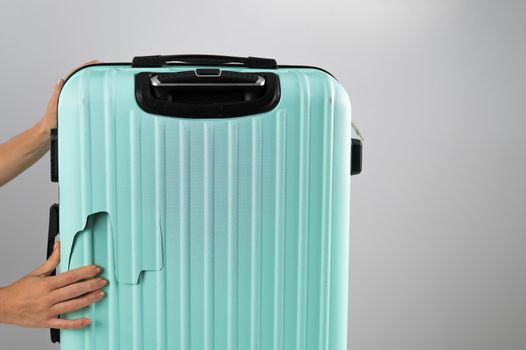 A woman demonstrates a broken suitcase on a white background. Damaged baggage during the flight