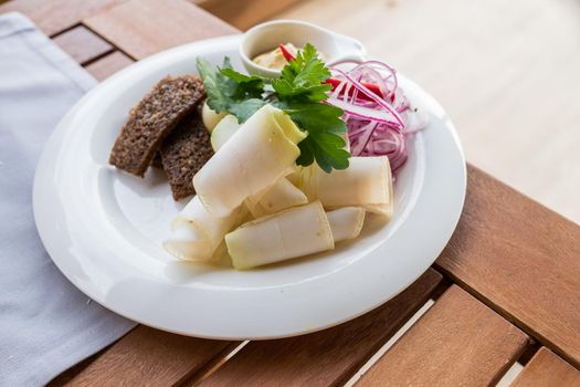 Fat. Snack for vodka. On a cutting board is a composition of pickles, red onions, fried bread and garlic. On a wooden table in a beer pub