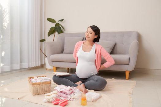 Happy young mother with travel luggage of baby clothes at home