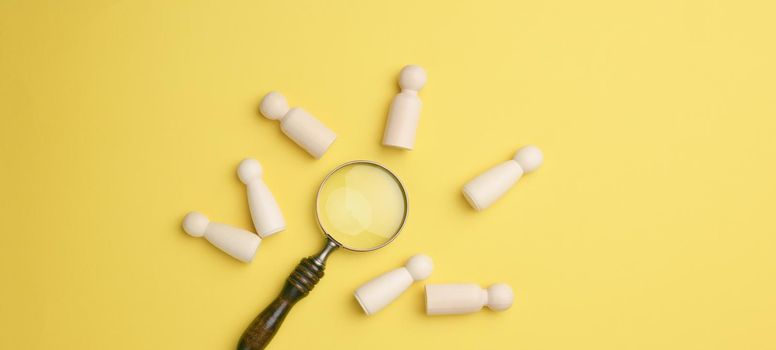 wooden men and a magnifying glass on a yellow background. Recruitment concept, search for talented and capable employees, career growth, flat lay