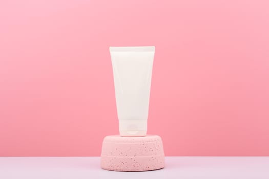 White plastic cosmetic tube with cream, balm, mask, scrub or lotion on pink pedestal against pink background with copy space. Concept of natural organic skin care products 