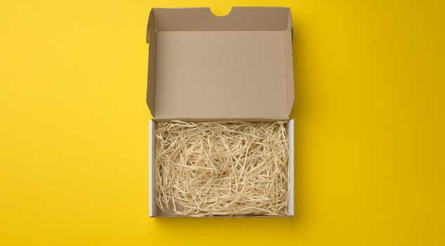 rectangular open corrugated paper box with sawdust inside. Packaging, containers for transportation on a yellow background